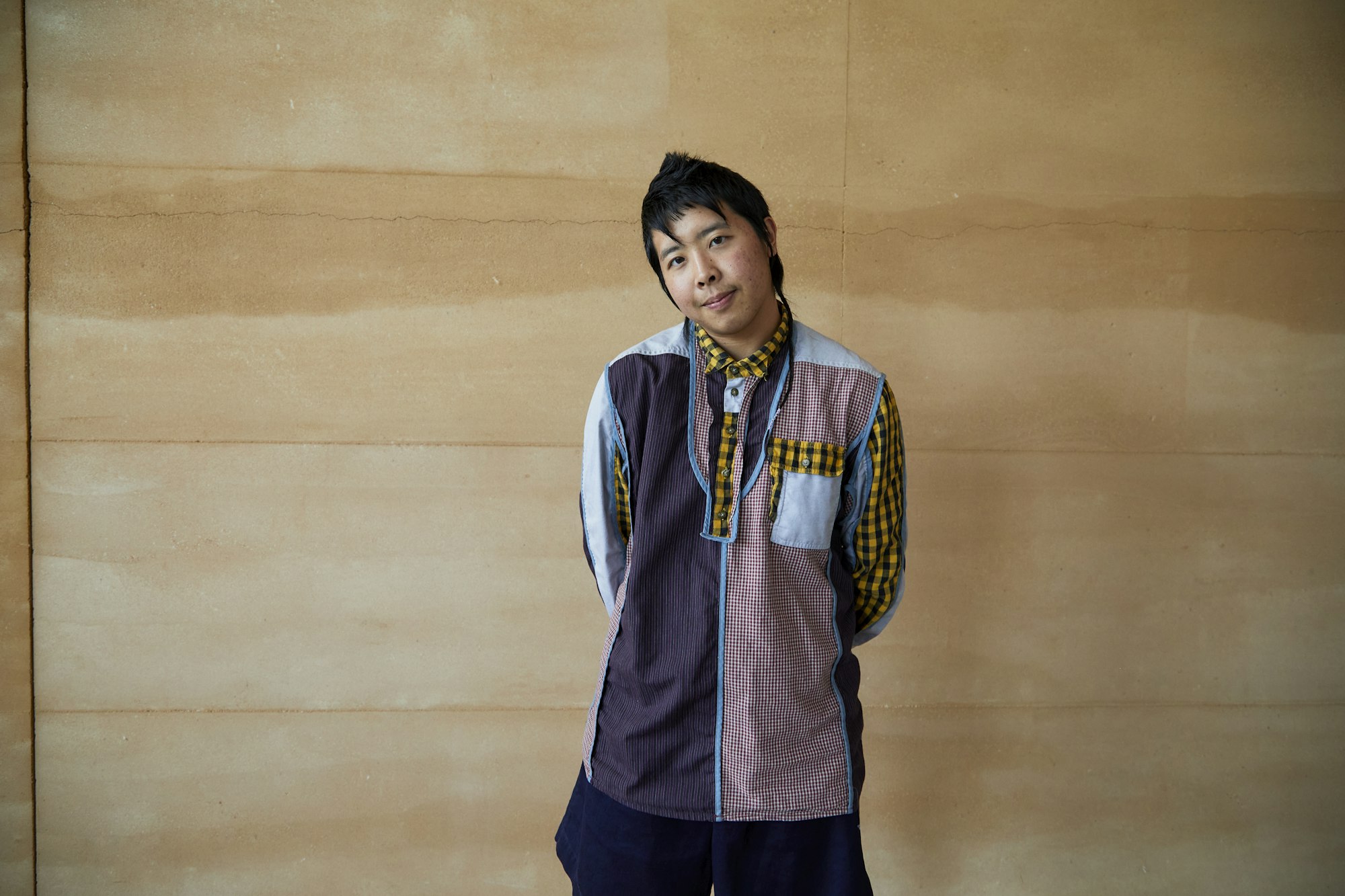 A person with short black hair and light brown skin stands with their head slightly tilted to the left.