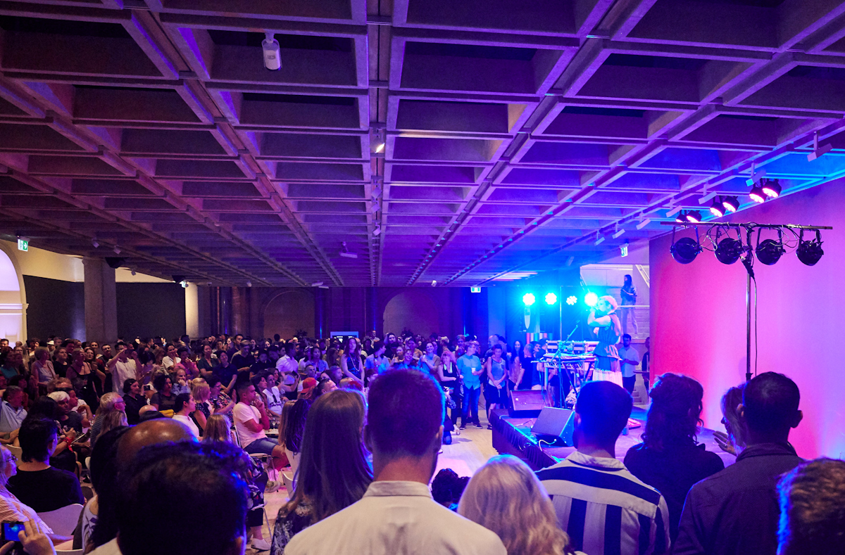 Many visitors watching a performance in the entrance court of the Gallery at night.