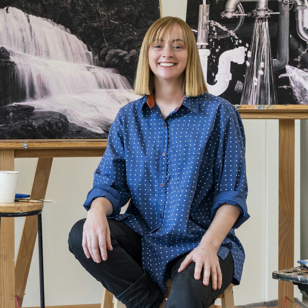 A person sits on a stool between artworks on easels