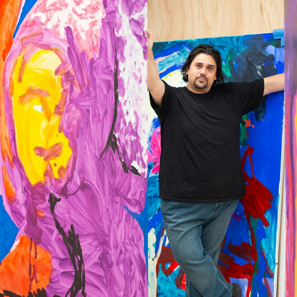 A person stands between large brightly coloured paintings