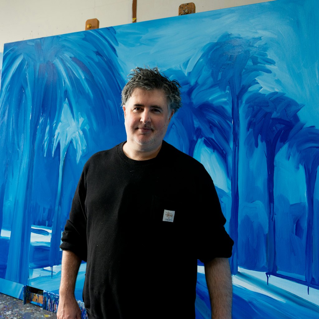 A person stands before a large blue painting of trees