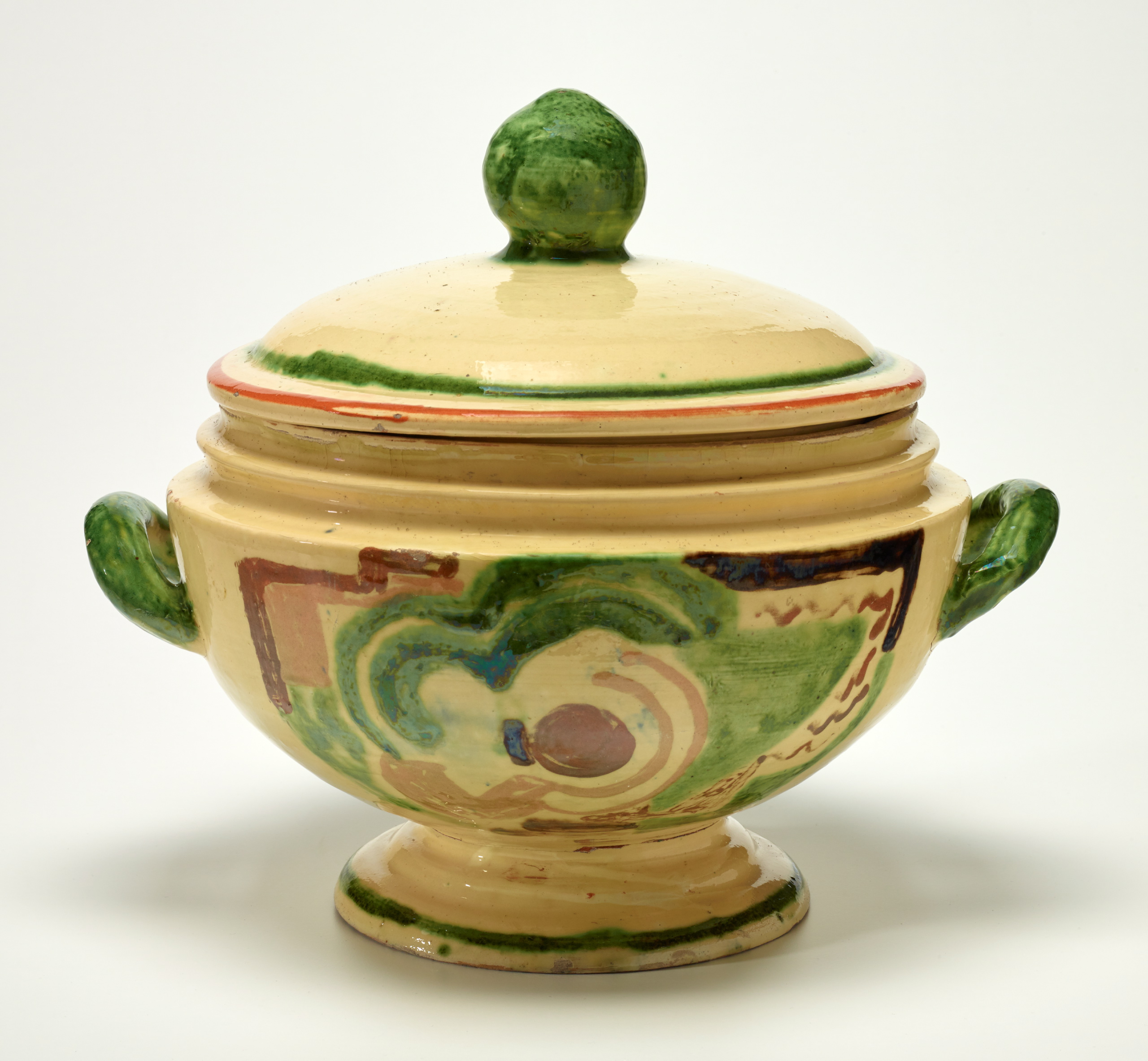 A glazed earthenware tureen with grass green handles and a brown and green illustration along the outside..