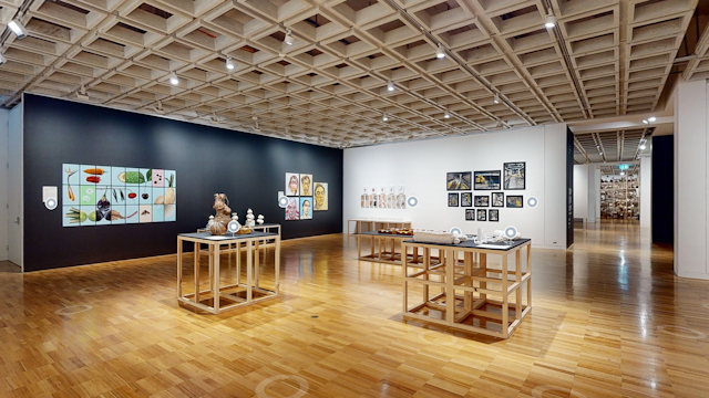 A gallery room with artworks on the walls and on five wooden plinths.