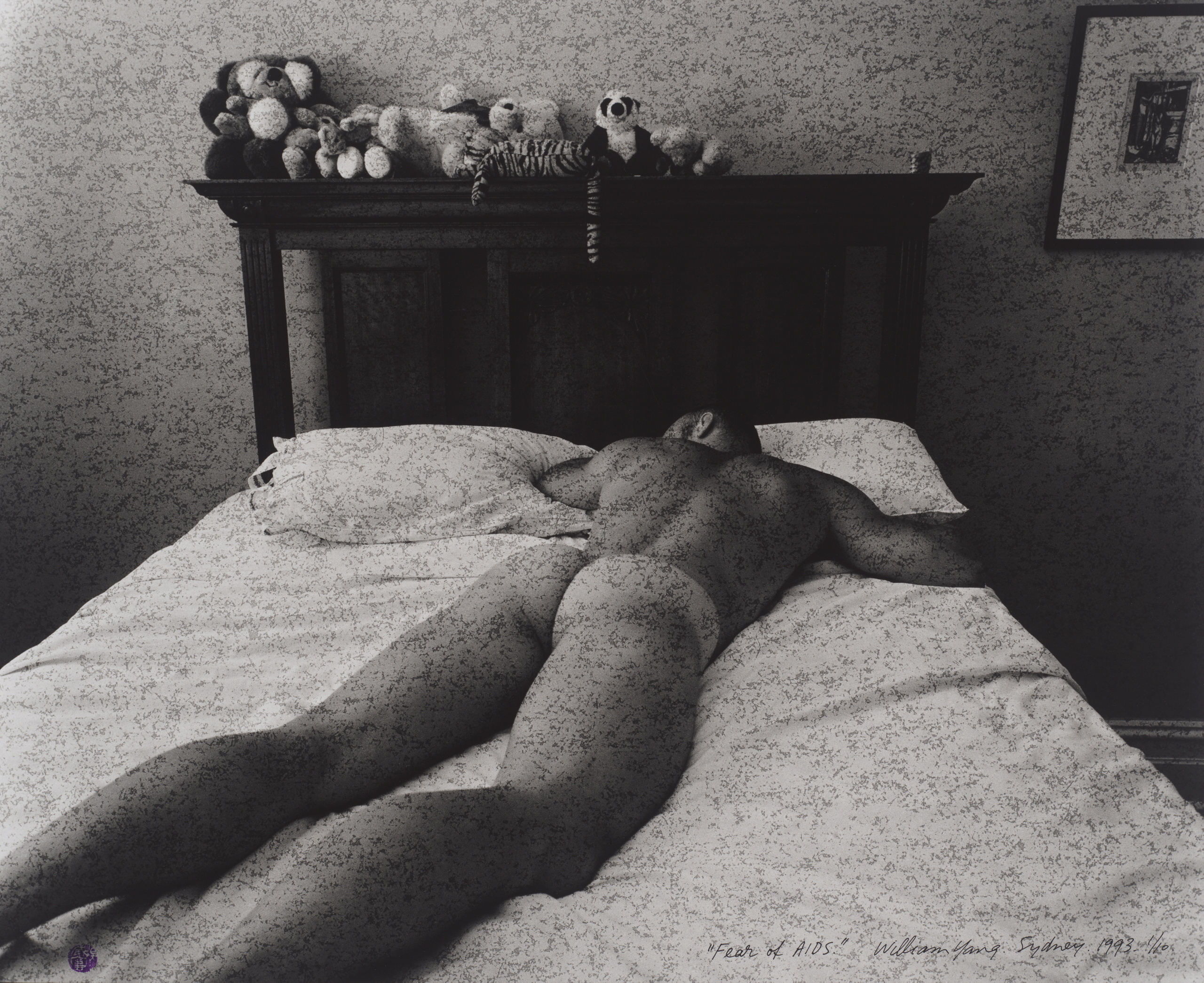 A black and white photograph of a naked person lying face down on a bed.