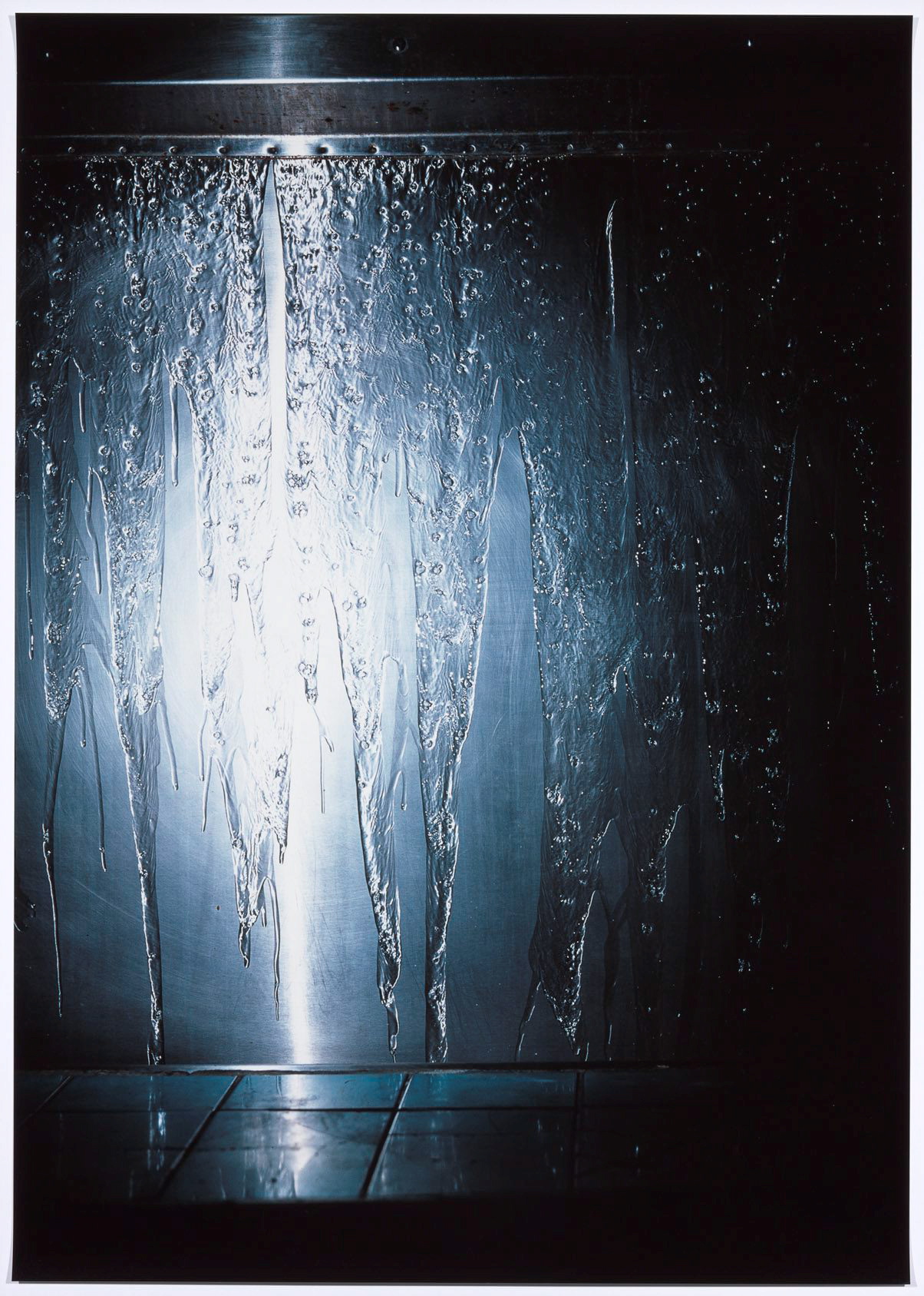 A photograph of liquid streaming down a urinal lit up by the cold flash of a light..