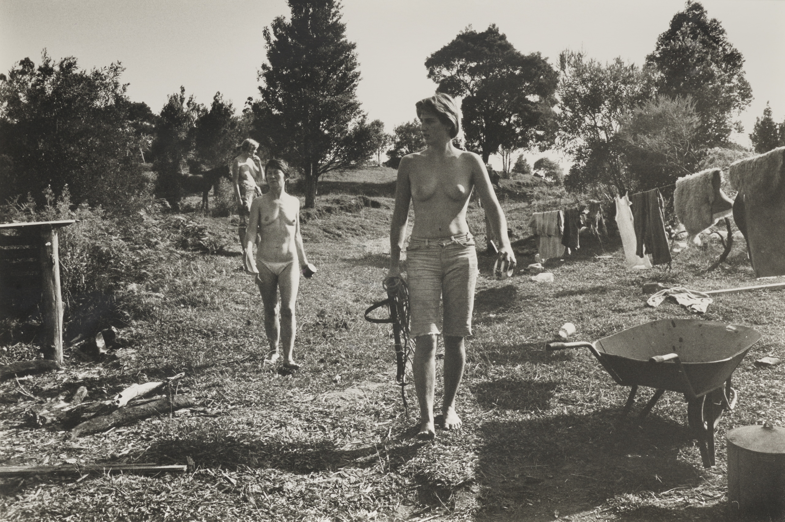 A black and white photograph of three bare-breasted people walking through a field.
