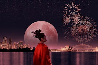 A person in red with a citscape in the distance, a huge full moon and fireworks