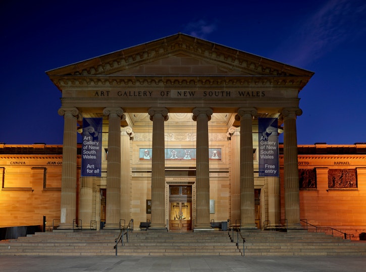 A view at night of a large sandstone building with a classical columned portico