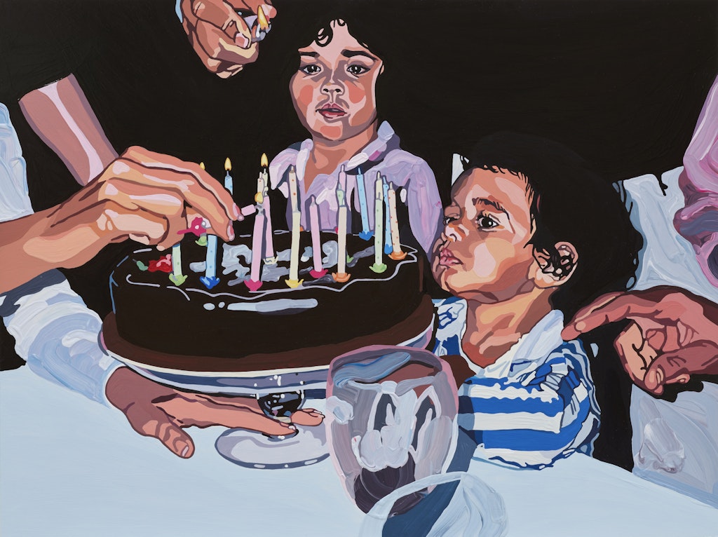 Two children look at candles on a birthday cake with adult hands around them