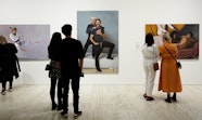 People stand in front of three large portrait paintings on a gallery wall