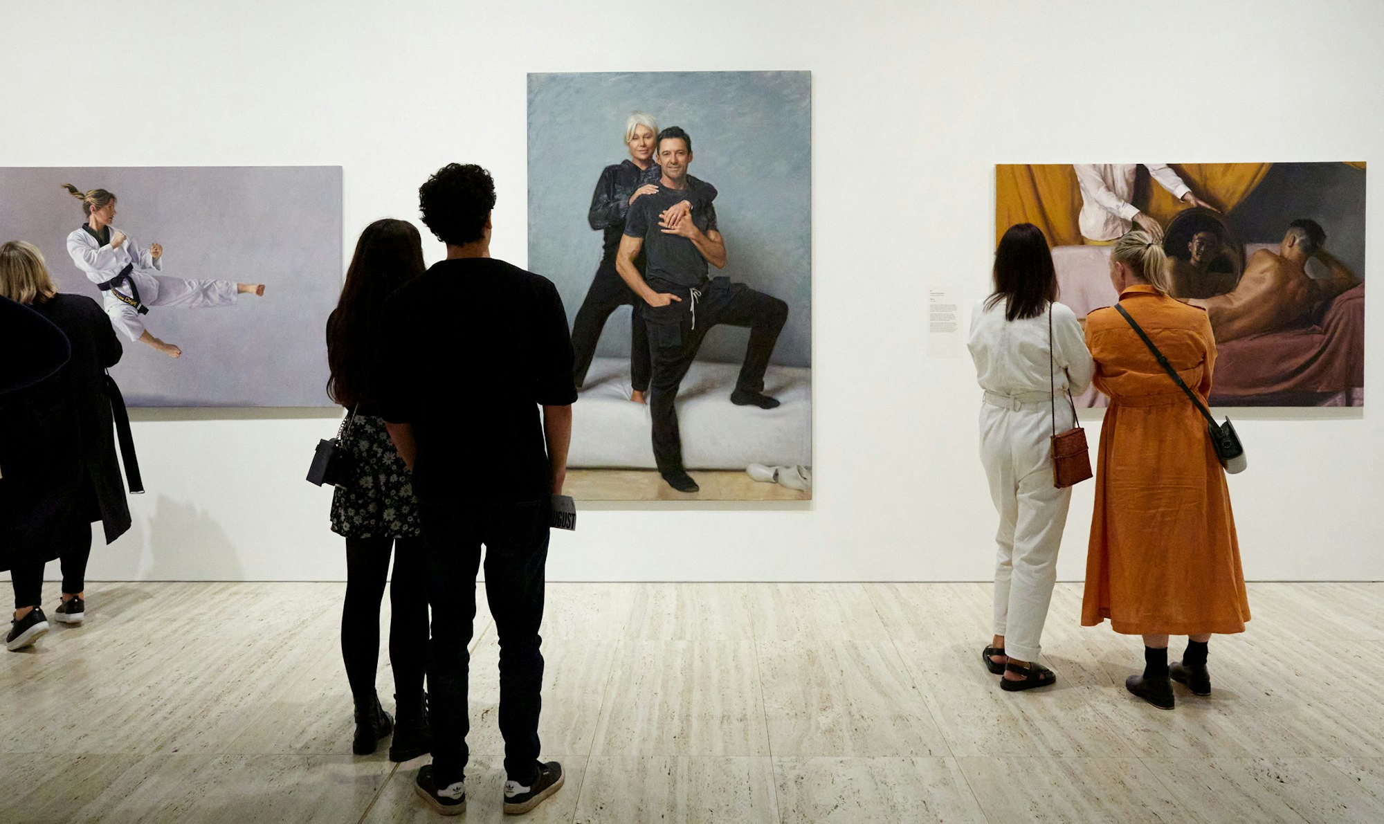 People stand in front of three large portrait paintings on a gallery wall