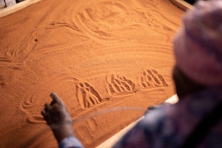 Elder Ngilan Dodd marking storylines in the sand for Robert Fieldings’s Milpatjunanyi 2022 © Mimili Maku Arts, photo: Meg Hansen