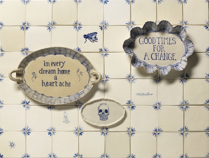 Square ceramic titles on which two ceramic oval discs read 'Chaos reigns' and 'In every dream home a heartache'