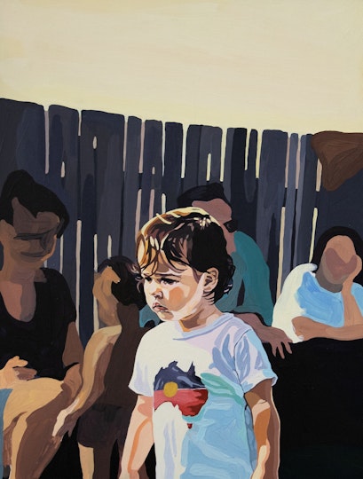 A child wearing a t-shirt with the Aboriginal flag. In the background, people sit beside a fence