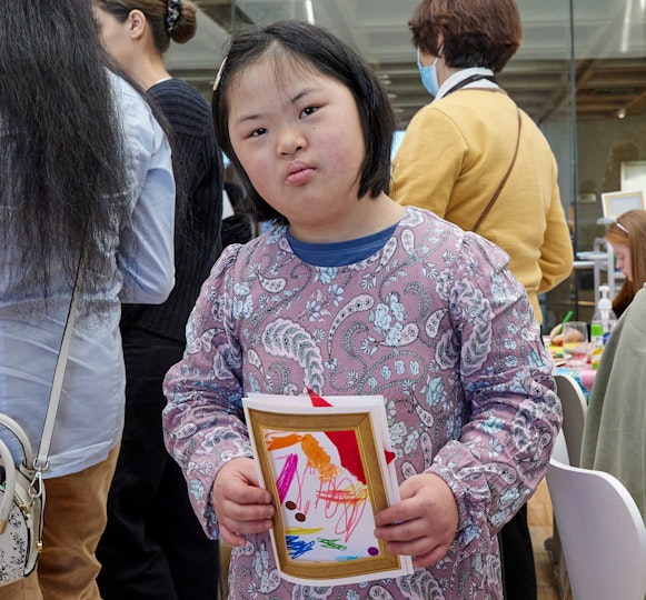 A young person holds a small artwork made on folded paper