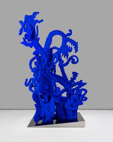 A bright blue sculpture of interlocking abstract shapes on a small wedge-shaped plinth