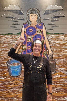 A person stands in front of a painting with their fist raised