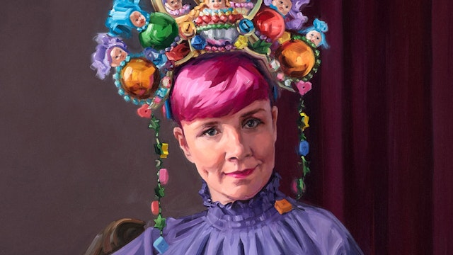 A person with pink hair in a high-necked purple outfit wearing a large colourful headpiece