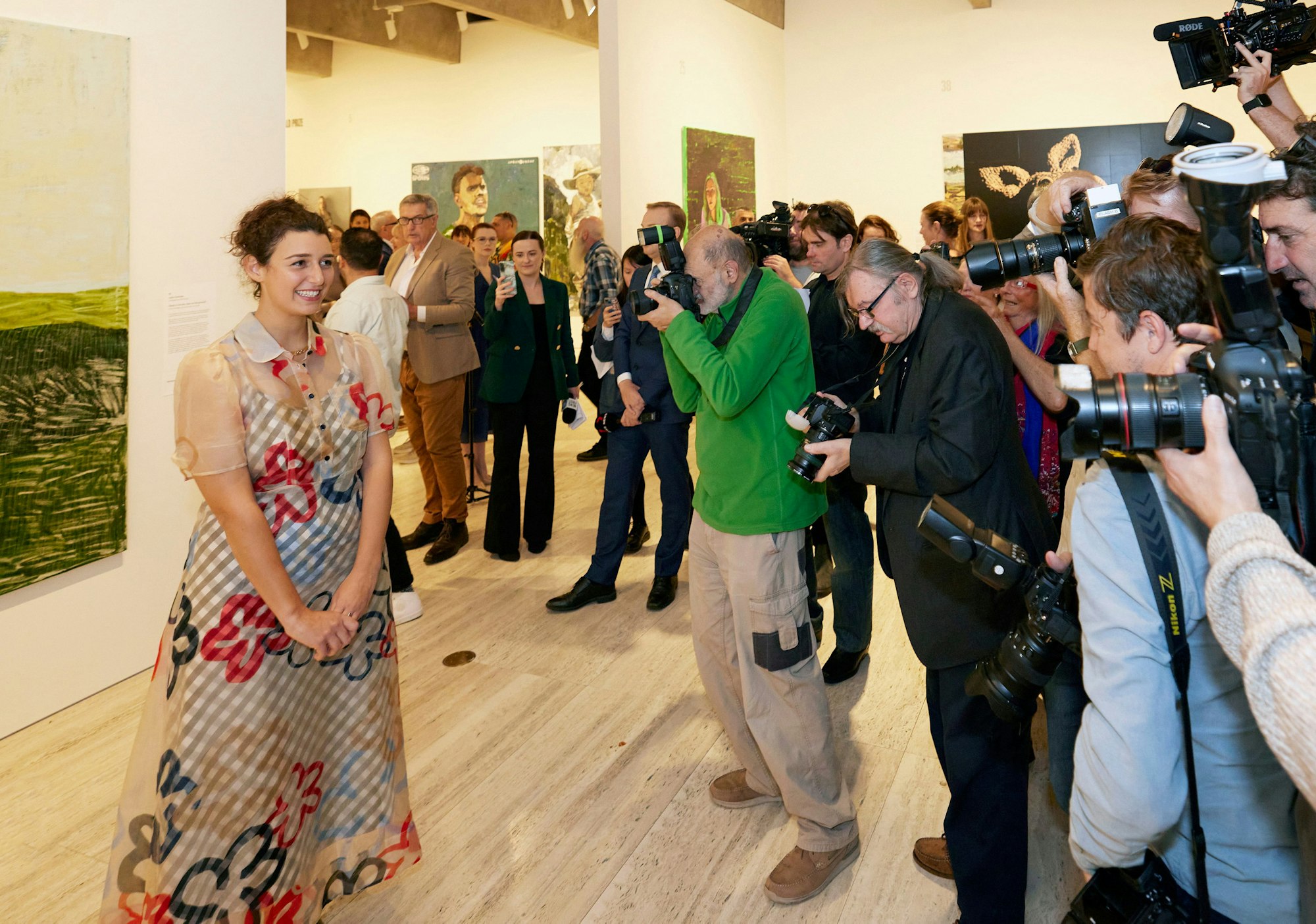 A person stands next to a painting in front of a crowd of people with cameras