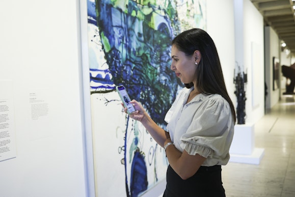 A woman standing in front of John Olsen's Five Bells while interacting with her mobile looking at the 70th anniversary art trail