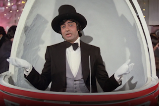 A person wearing a hat, gloves, shirt, bow tie, waistcoat and jacket inside a domed structure within a crowded room