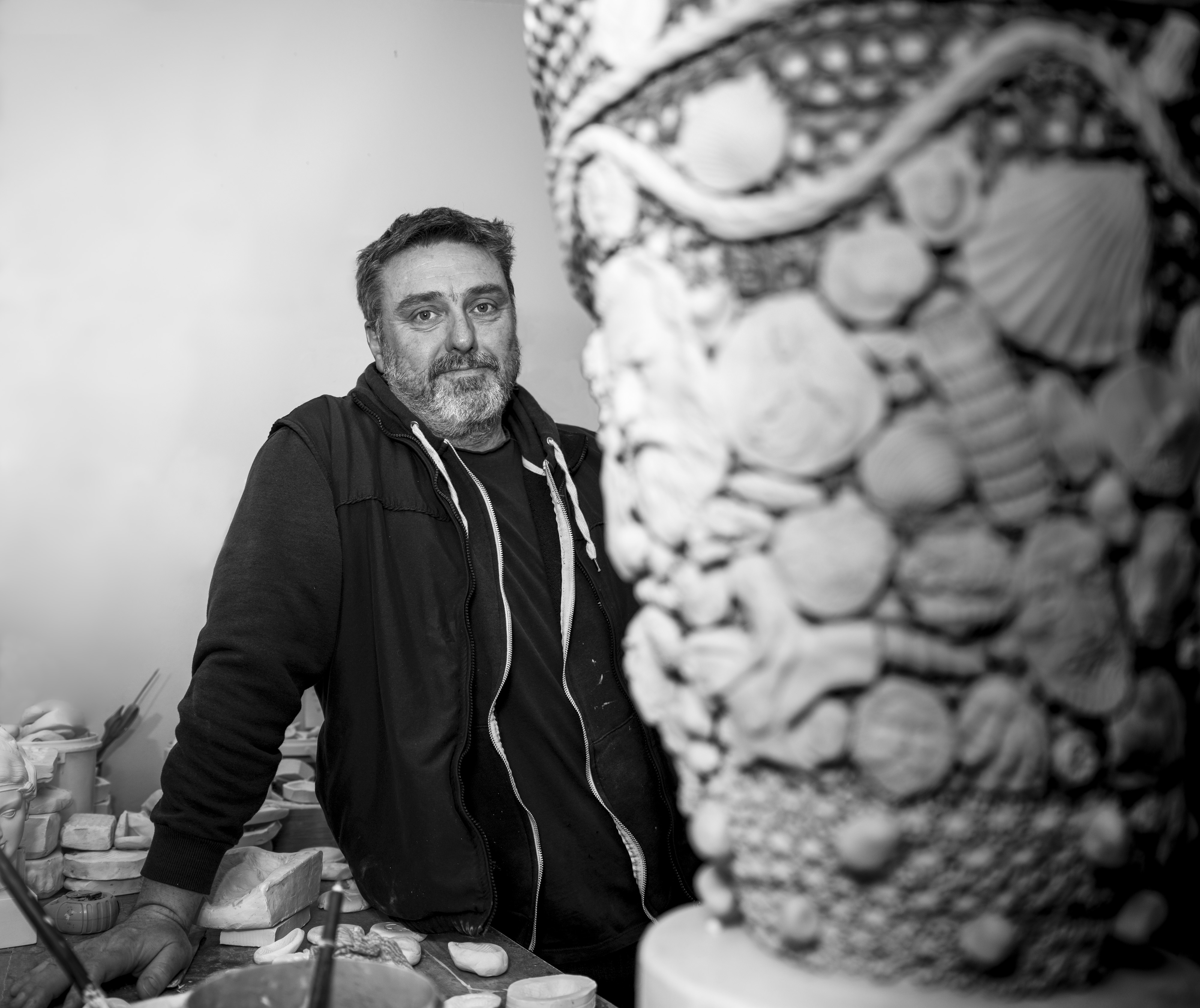 A person stands leaning on a workbench with a ceramic object in the foreground