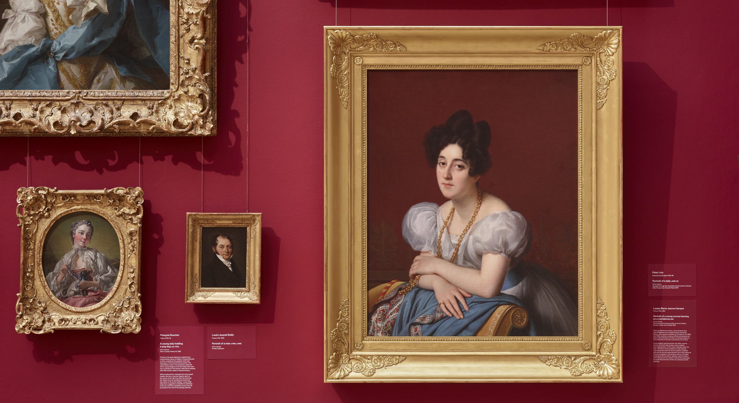 Gold-framed portrait paintings hanging on a red wall