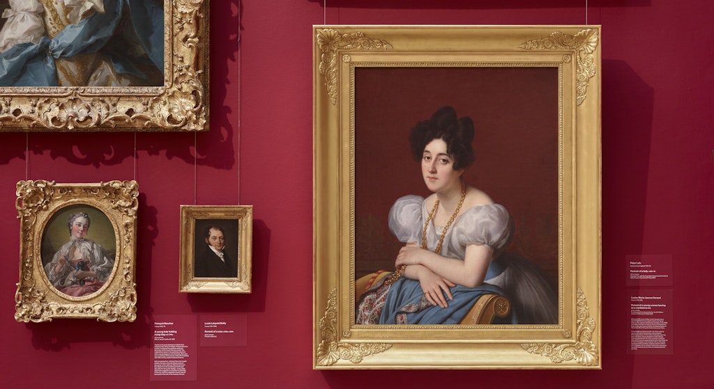 Gold-framed portrait paintings hanging on a red wall