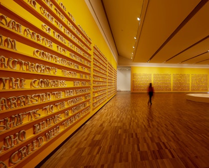 A person in a large room with many blocks of text on the yellow walls