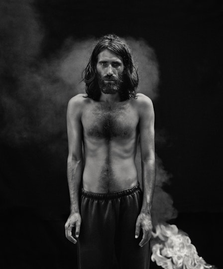 A person wearing trousers and no top stands with their hands hanging by their sides
