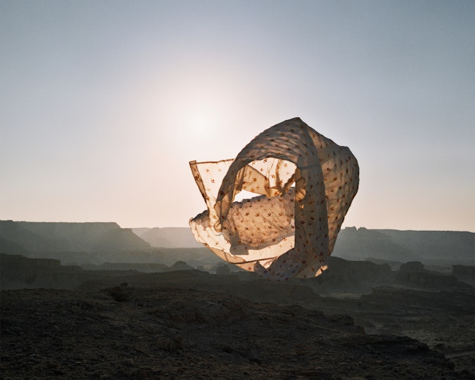 A figure within a long billowing piece of fabric within a desert landscape in half light
