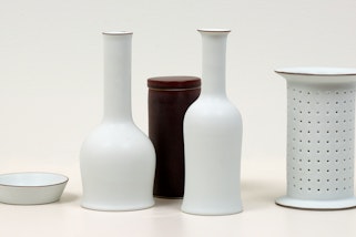 A group of five ceramic vessels of different shapes. Four are white and the other is dark.