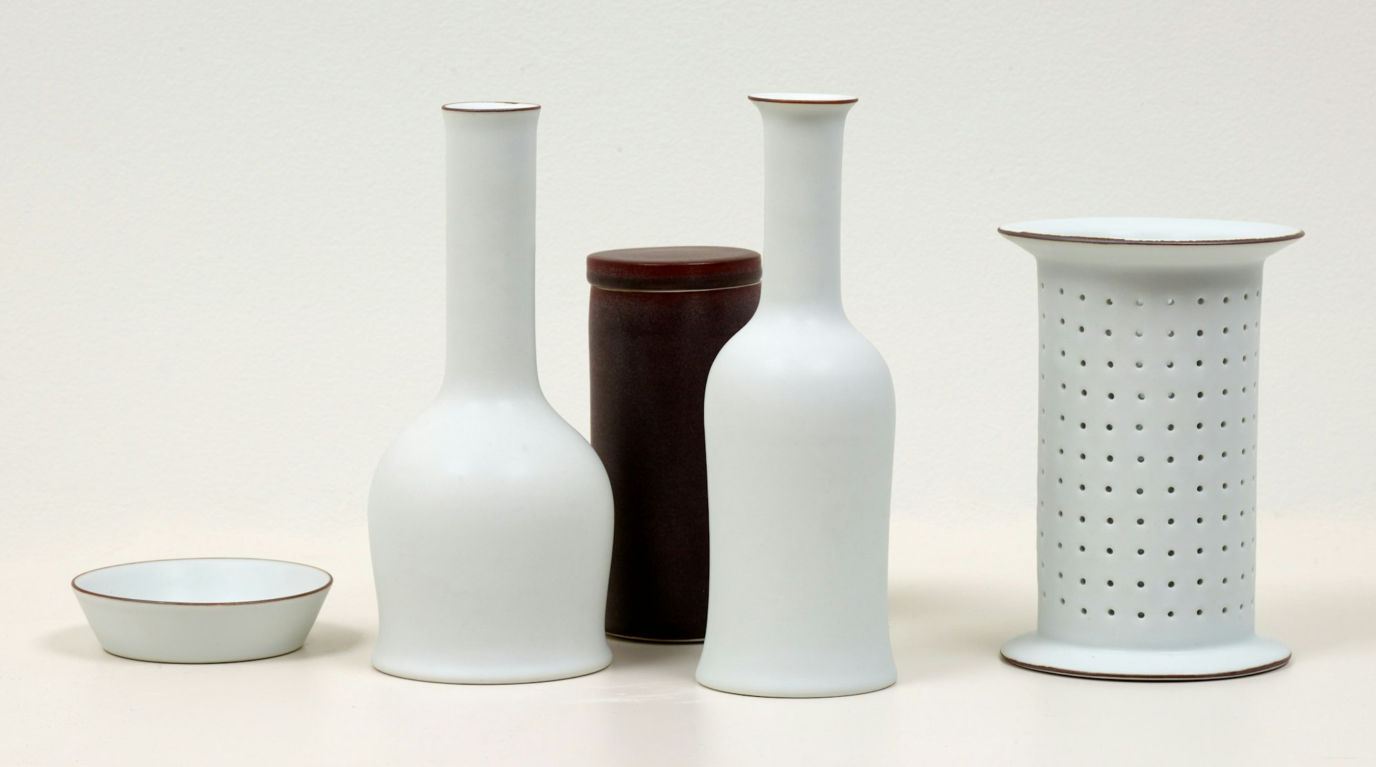 A group of five ceramic vessels of different shapes. Four are white and the other is dark.