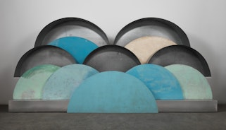 A sculpture of overlapping semi-circular shapes in shades of blue, grey, green and yellow