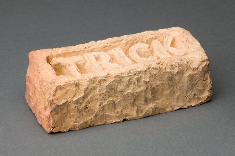 A rough-hewn brick with the word 'trick' embedded in the top