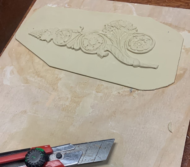 A carved ornament and a stanley knife lie on a wooden board