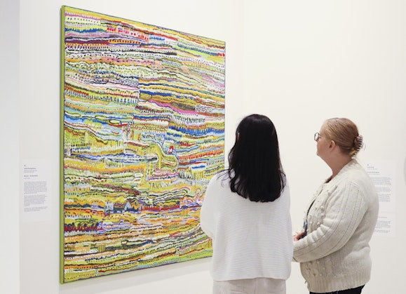 Two people look at a brightly coloured painting on a gallery wall