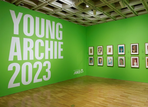 Two bright green walls. One has text 'Young Archie 2023. Presenting partner ANZ'. The other has 14 framed artworks.