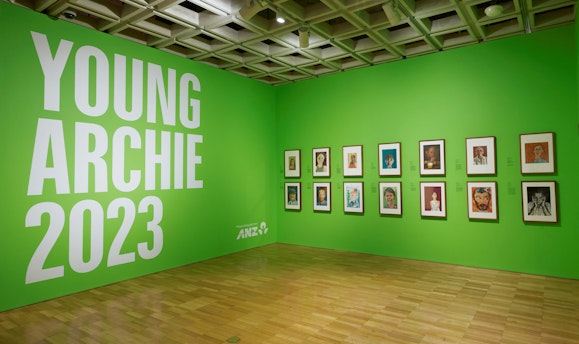Two bright green walls. One has text 'Young Archie 2023. Presenting partner ANZ'. The other has 14 framed artworks.
