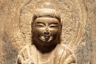 The face and upper torso of a stone buddha on a stone column