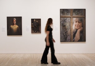 A person walks in front of a wall hung with three portrait paintings