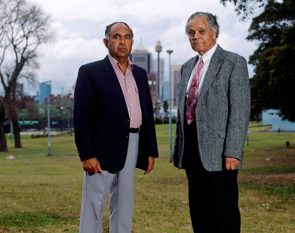 Two people stand in a park with tall buildings in the distance