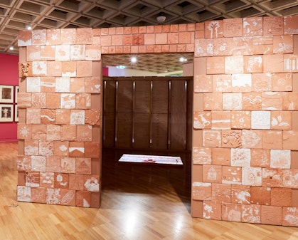 A box-like structure made of terracotta tiles with an entranceway. Inside a video is projected on the floor