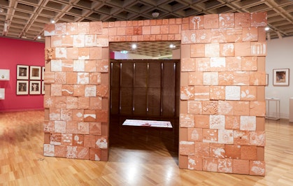 A box-like structure made of terracotta tiles with an entranceway. Inside a video is projected on the floor