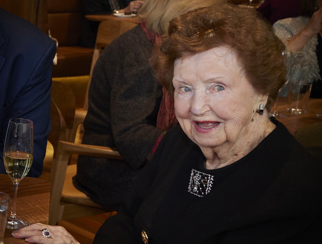 A red-haired person dressed in black sits with a glass of sparkling wine