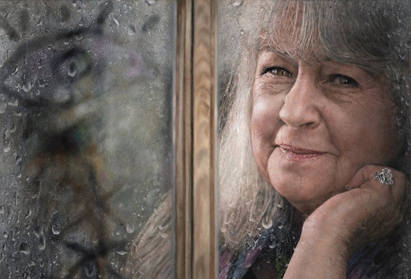 The head of a person, resting on one hand with a large ring, seen through a framed rain-flecked window pane