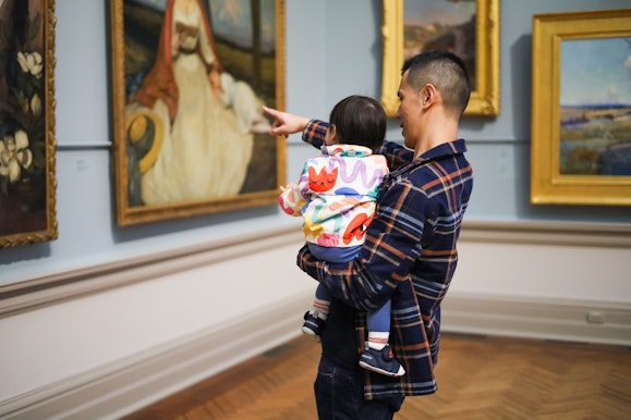 A person holding a small child looking at works in the Grand Courts at the Art Gallery of New South Wales