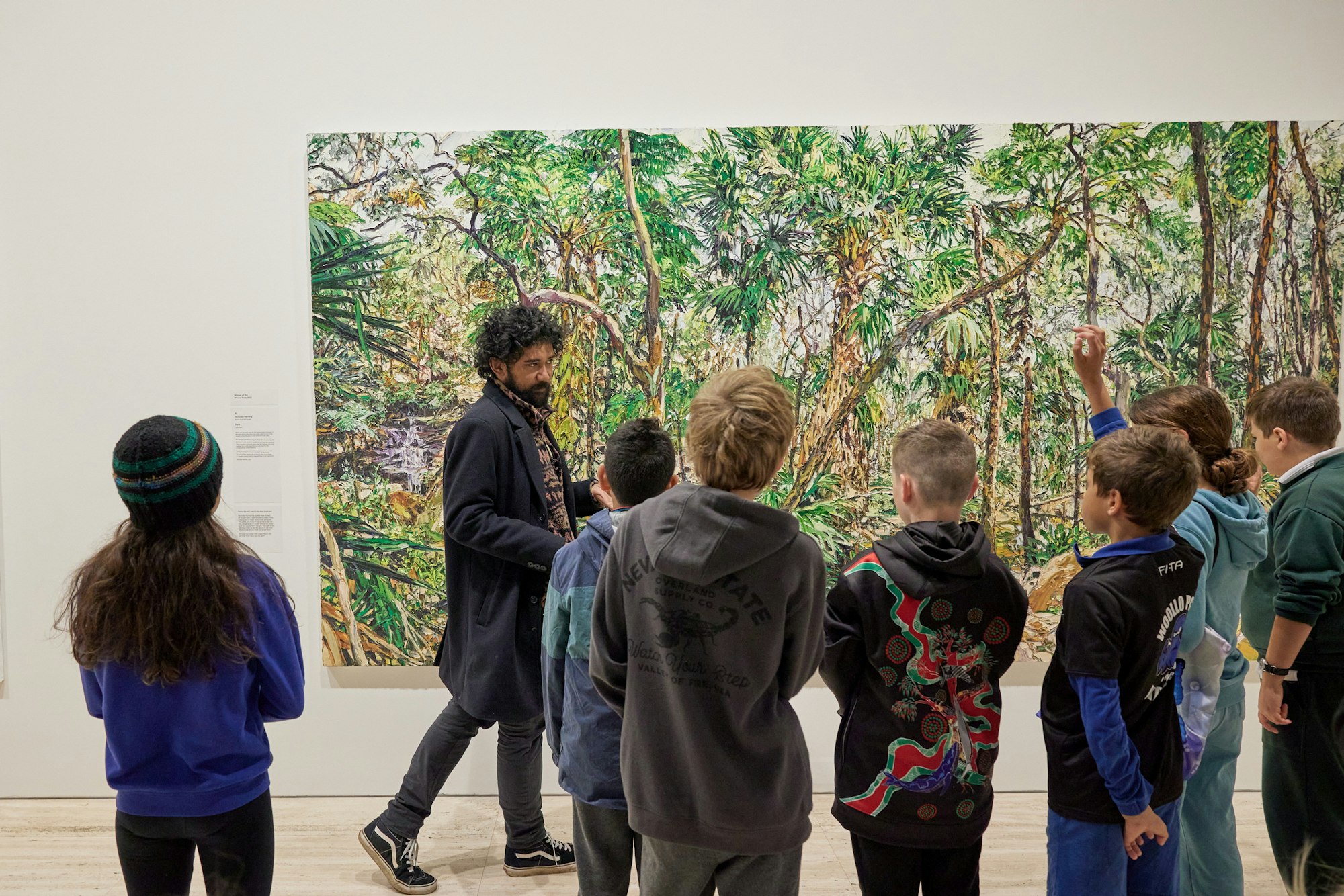A group of seven young students and an adult in front of a large painting of densely grown trees.