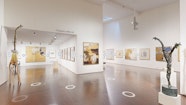 A large room with paintings hung white walls and several giraffe sculptures.