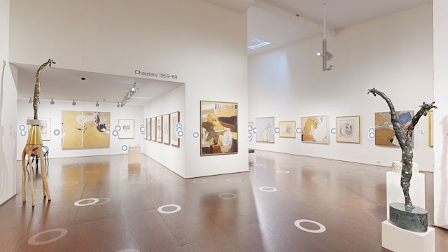 A large room with paintings hung white walls and several giraffe sculptures.